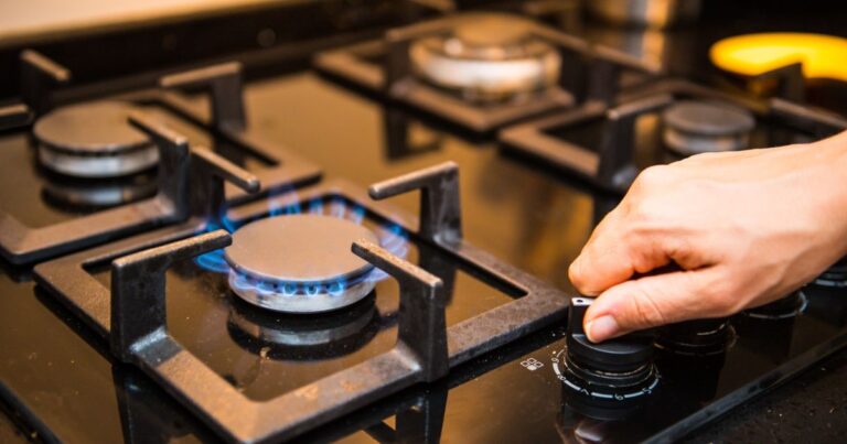 A hand lifting out a grill set on a gas range.