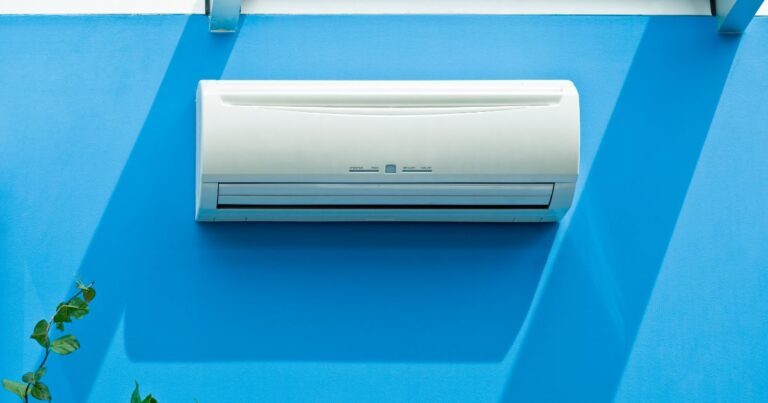A split type air conditioner installed on a blue wall. Above the wall is a glass ceiling that allows natural light to come in.