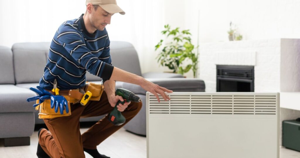 A man performing repairs on a heater unit in a living room. 