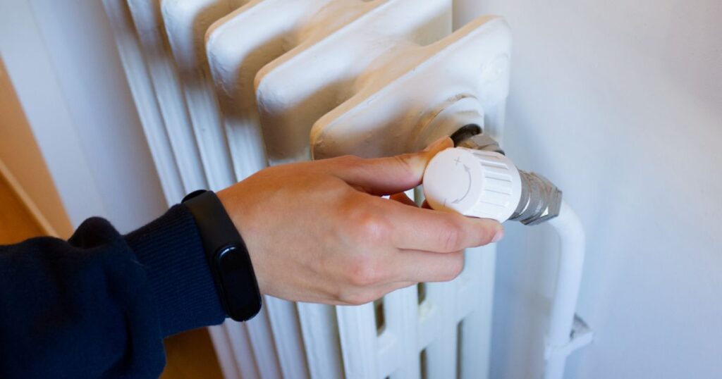 A hand turning a dial on a heater installed on the wall. 