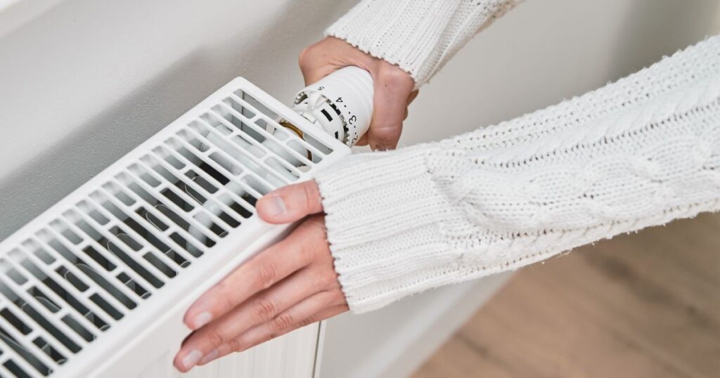 Hands with white sweater sleeves over them testing out a heater. 