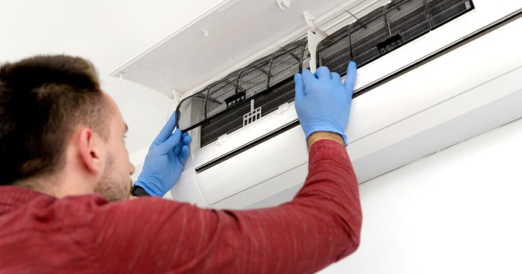 A man wearing blue rubber gloves, attaching clean air filter into a split type airconditioner. 