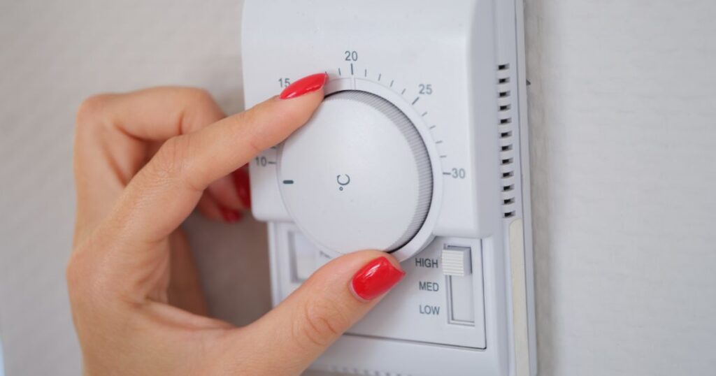 A manicured hand turning the dial of an air conditioning system to the left.