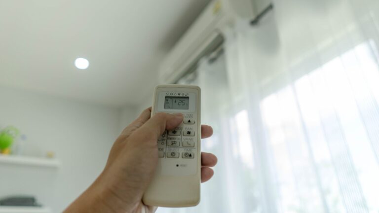 A hand holding an air conditioner remote upwards.