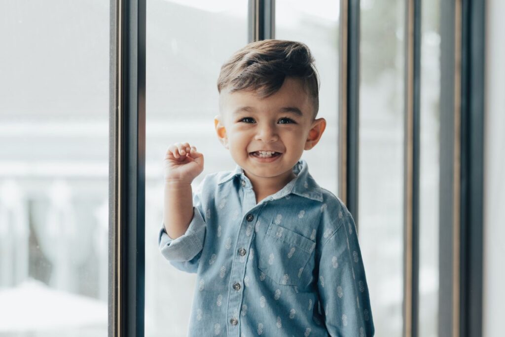 A little boy smiling as he leans on a glass sliding door in their home.