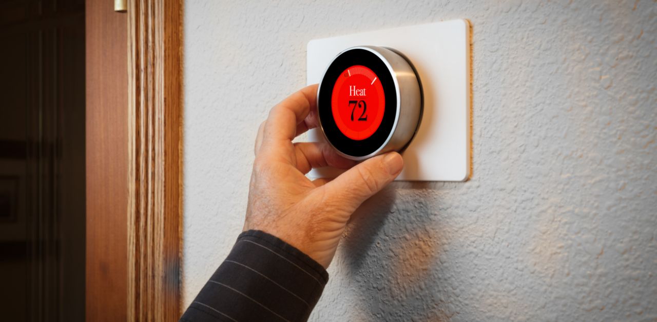 A hand dialing up the heating system on a home heating controller installed on the wall.