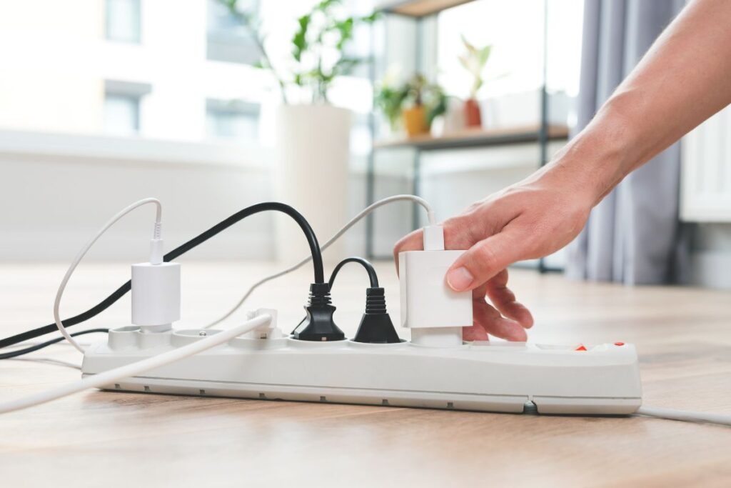 A hand plugging in a charger to an already overloaded extension wire. This may cause an overloaded circuit.