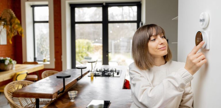 A woman adjusting the settings in her home's heating and cooling system thermostat.