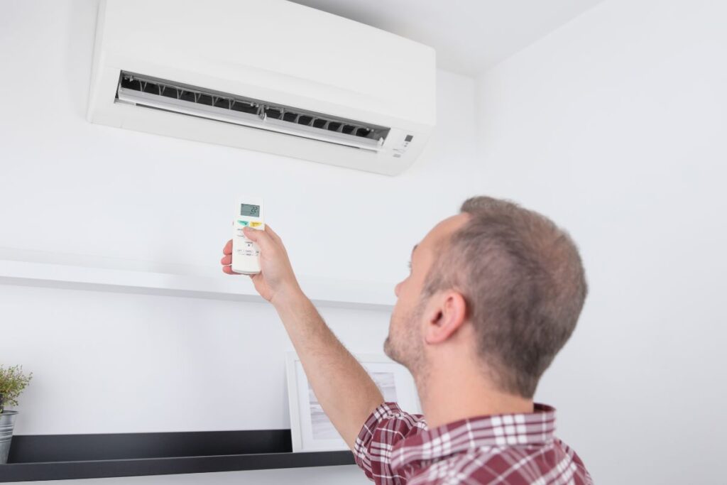 A man turning on a split type AC in a place with white walls. The AC unit appears to be clean and well maintained, on par with the  Complete AC Tune-Up Checklist for Homeowners.