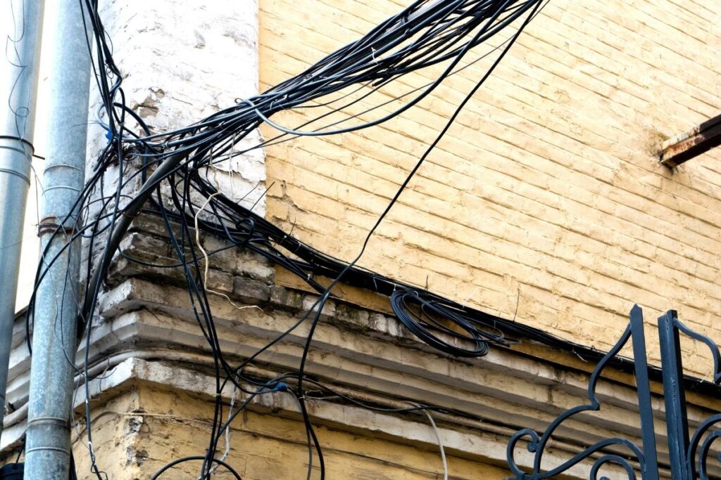 An example of the hidden dangers of old home wiring. This is image shows clusters of old home wiring attached to the brick walls of a home.