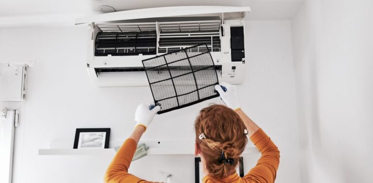 A woman in an orange overall replacing the filter in a split type air conditioner. The value of a professional air conditioner cleaning service lies in the prolonged lifespan of an air conditioning unit.