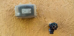 A socket outdoors with a protective cover beside a faucet. Doing this is one of the best ways on how to stay safe around electricity in wet areas.