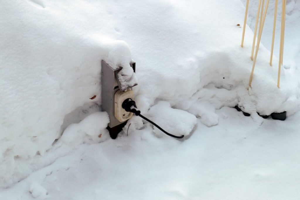 An electric plug in a socket outdoors, covered with snow. Covering this is one of the ways on how to stay safe around electricity in wet areas.