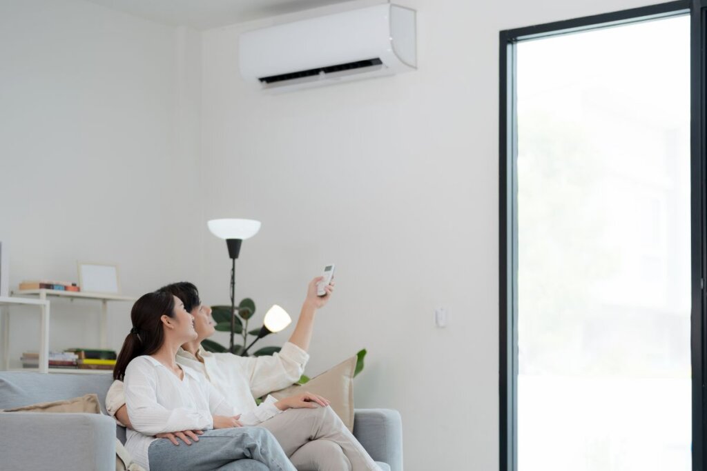 A couple in a living room. The man is holding a remote control, turning on a split type AC with proper refrigerant levels.