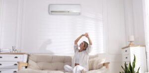 A woman happily sitting down in a living which appears to be cooled by a split type airconditioner.