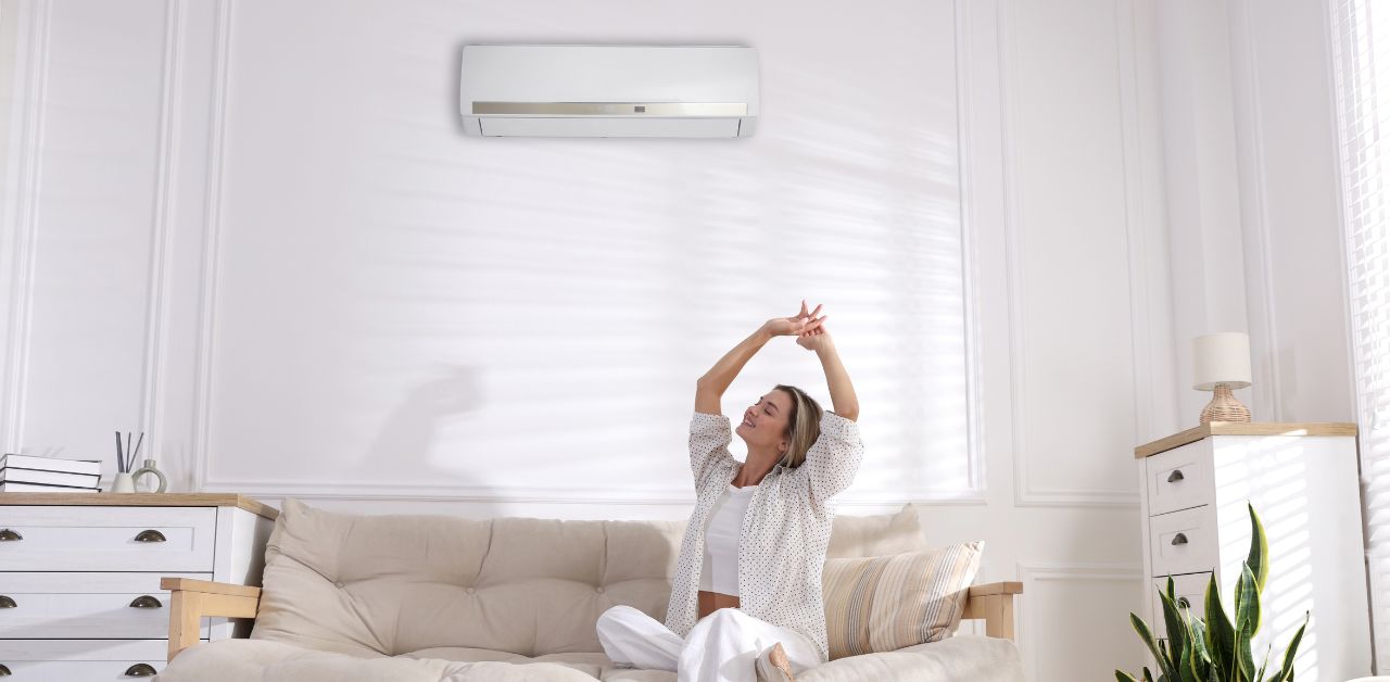 A woman happily sitting down in a living which appears to be cooled by a split type airconditioner.