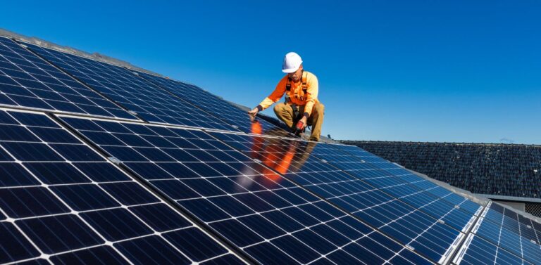 A man in orange uniform and protective gear installing a solar power system on a roof during daytime.